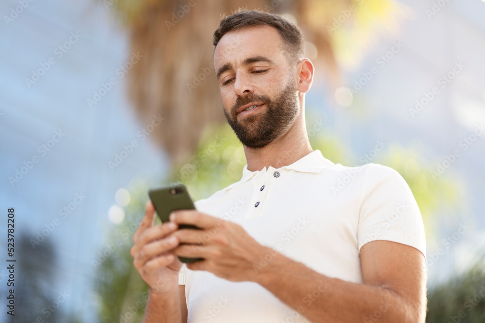 Confident handsome latin man using mobile app shopping online on the street. Bearded businessman holding smartphone checking email, searching information. Modern technology, e-commerce concept Confident handsome latin man using mobile app shopping online on the street. Bearded businessman holding smartphone checking email, searching information. Modern technology, e-commerce concept