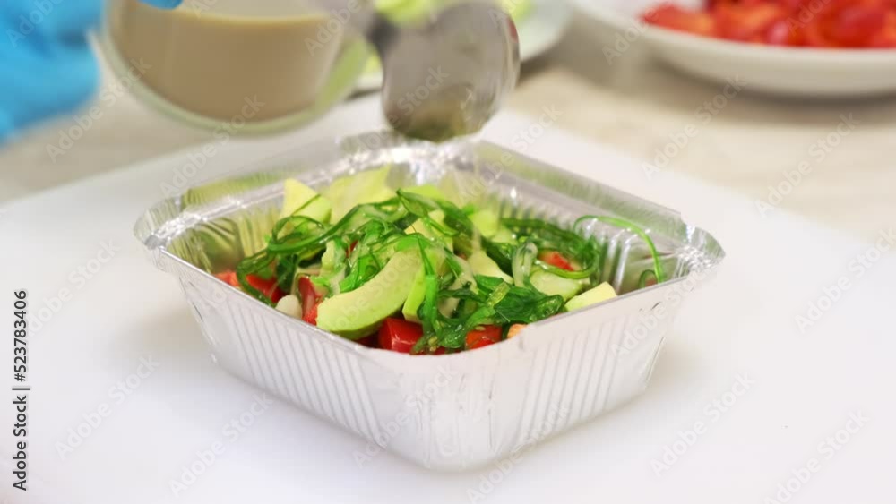 Chef hands, dressing sauce pouring in a vegetable salad with avocado and hiyashi seaweed close up. Healthy and dietary food delivery. Preparing healthy meals in a container box on professional kitchen Chef hands, dressing sauce pouring in a vegetable salad with avocado and hiyashi seaweed close up. Healthy and dietary food delivery. Preparing healthy meals in a container box on professional kitchen