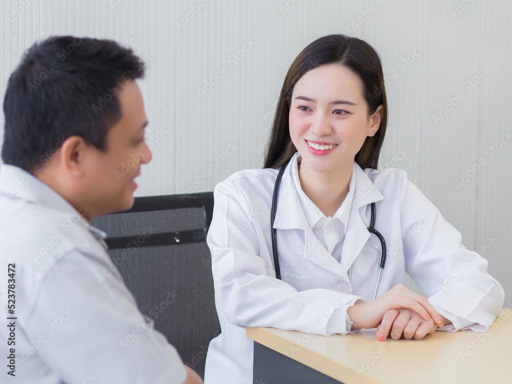 Professional beautiful young Asian female doctor talking with a man patient about his pain and symptom while they put on a face mask Thermometer on table at the examination room in hospital. Professional beautiful young Asian female doctor talking with a man patient about his pain and symptom while they put on a face mask Thermometer on table at the examination room in hospital.