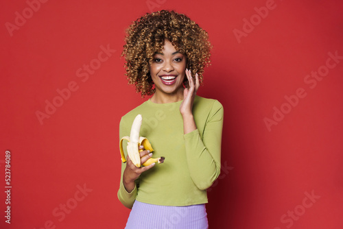 Young black woman with afro hairstyle laughing while eating banana