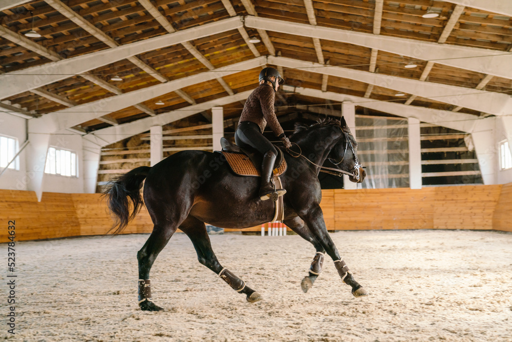 Jockey woman wearing helmet riding her horse during equestrian practice Jockey woman wearing helmet riding her horse during equestrian practice