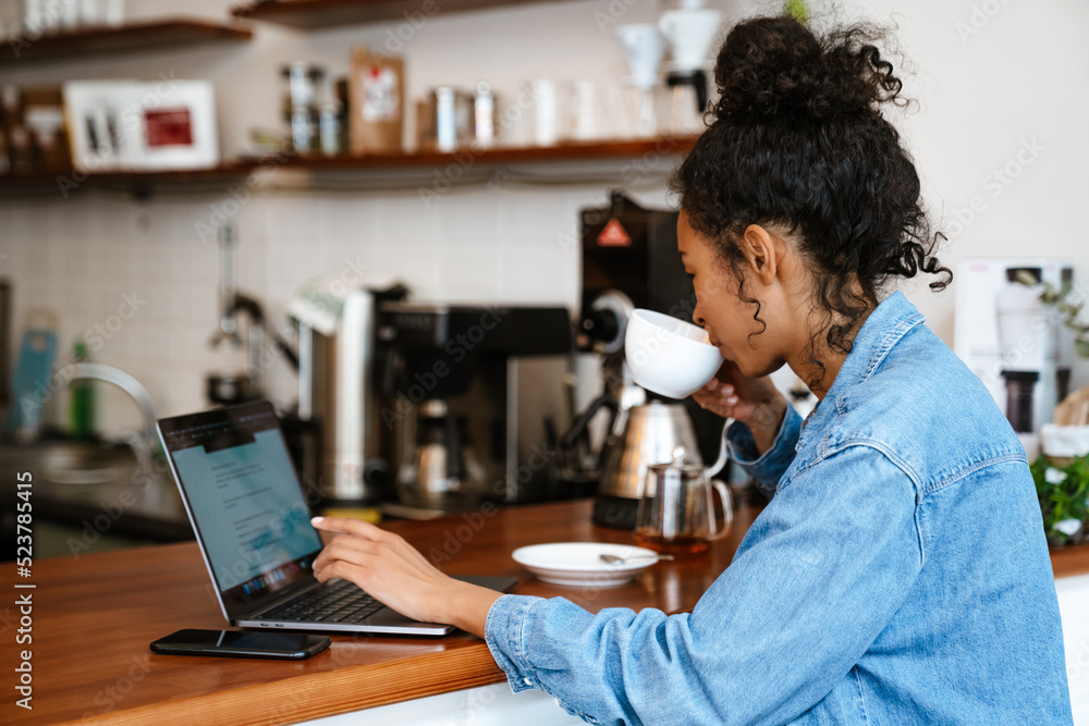 Black young woman drinking coffee while working with laptop in cafe
