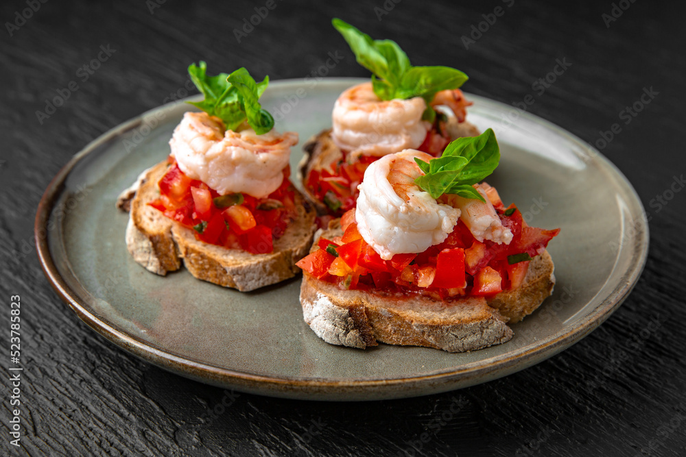 Healthy nutritious breakfast of bruschetta with tomatoes, shrimp and basil in a ceramic plate on a dark textured background. Restaurant menu Isolated on black