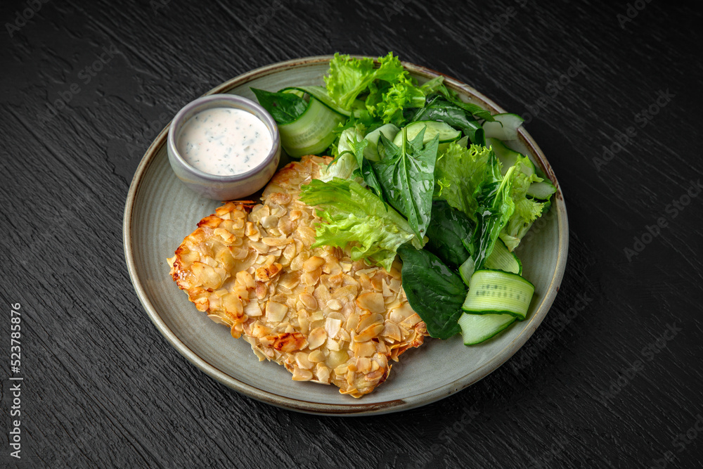 Chicken schnitzel in almond flakes in a ceramic plate on a dark textured background. Restaurant menu Isolated on black Chicken schnitzel in almond flakes in a ceramic plate on a dark textured background. Restaurant menu Isolated on black