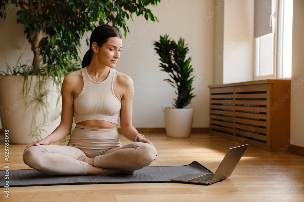 Young white woman using laptop during yoga practice on mat Young white woman using laptop during yoga practice on mat