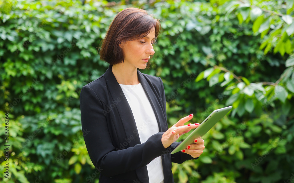 business woman uses a tablet against the background of green plants. portrait of a business woman with a tablet business woman uses a tablet against the background of green plants. portrait of a business woman with a tablet
