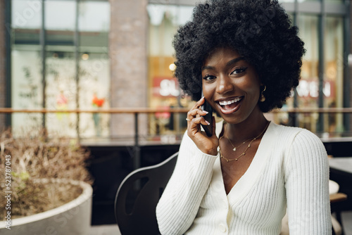 Smiling young african woman talking on cellphone at cafe