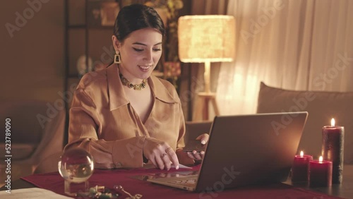 Waist up slowmo of young Middle Eastern fortune teller laying out tarot cards to client during online video seance on laptop photo