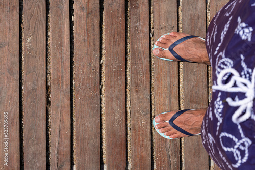Mans feet in flip flops on wooden boardwalk. Top view. Flat lay. Empty space, for text