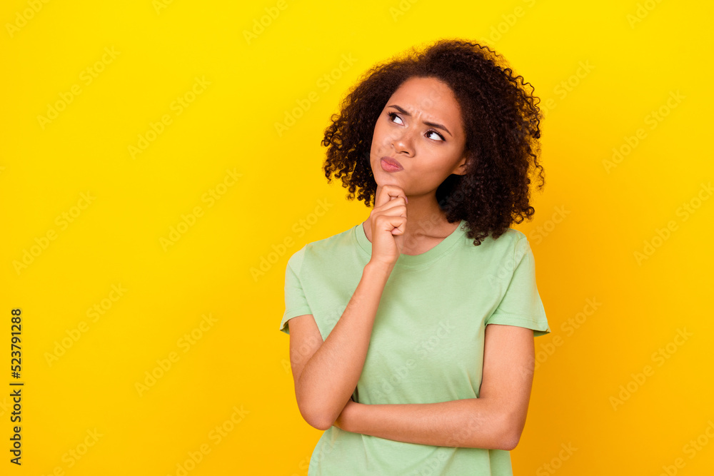 Photo of doubtful unsure girl dressed green t-shirt arm chin looking empty space isolated yellow color background Photo of doubtful unsure girl dressed green t-shirt arm chin looking empty space isolated yellow color background