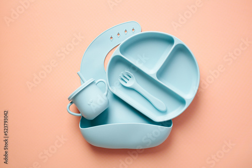 Flat lay composition with silicone baby bib and dishware on peach color background. Serving baby food concept. Flat lay, top view photo