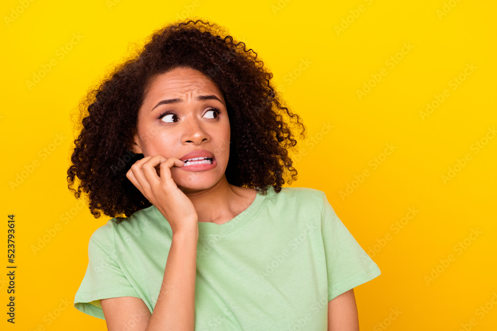 Photo of scared shocked girl dressed green t-shirt looking empty space biting fingers isolated yellow color background Photo of scared shocked girl dressed green t-shirt looking empty space biting fingers isolated yellow color background