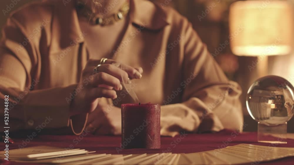 Cropped slowmo of unrecognizable fortune teller putting out wax candle with fingers sitting at table with tarot spread on red velvet cloth Cropped slowmo of unrecognizable fortune teller putting out wax candle with fingers sitting at table with tarot spread on red velvet cloth