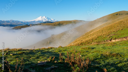 Misty autumn hills in front of distant snowy mountain