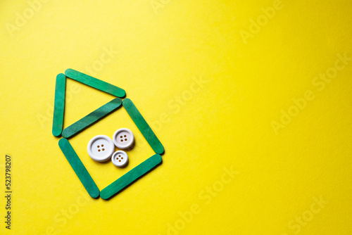 house from wooden green sticks on a yellow background, free space. Buttons of different sizes as a symbol of the family. Family in the house.