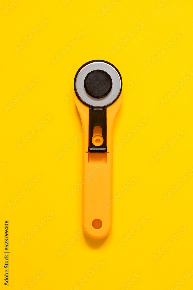 Yellow black rotary knife for patchwork on a yellow background. Sewing tool. Top view. Copy space. Yellow black rotary knife for patchwork on a yellow background. Sewing tool. Top view. Copy space.