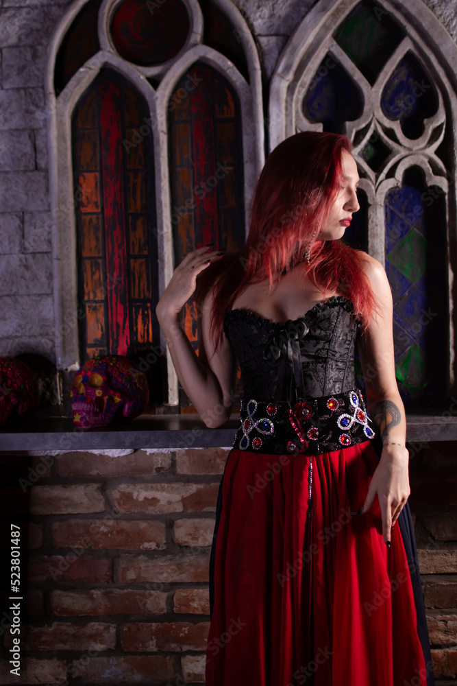 Beautiful young sexy woman vampire in medieval dark castle. Red gothic evening dress with corset.