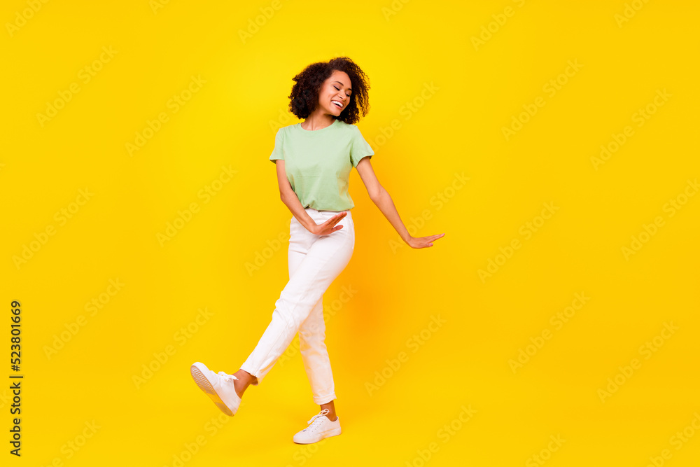 Full length photo of dreamy shiny lady wear green t-shirt walking dancing empty space isolated yellow color background