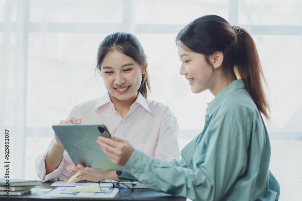 Smiling young Asian businesswomen talking to colleague and exchanging ideas together at office. Smiling young Asian businesswomen talking to colleague and exchanging ideas together at office.