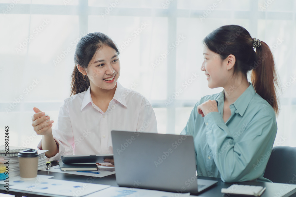 Smiling young Asian businesswomen talking to colleague and exchanging ideas together at office. Smiling young Asian businesswomen talking to colleague and exchanging ideas together at office.
