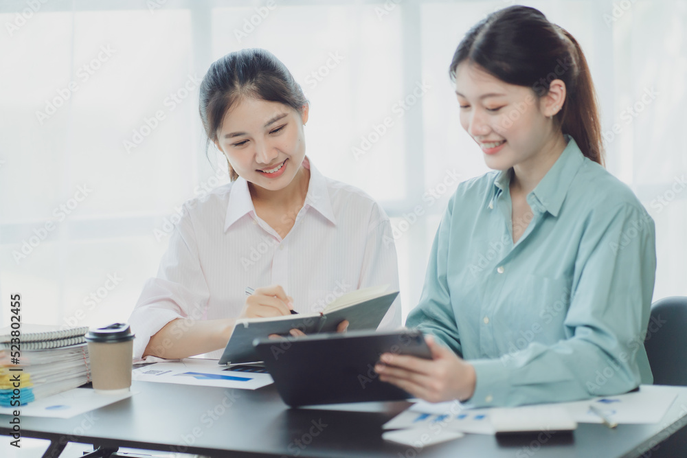 Smiling young Asian businesswomen talking to colleague and exchanging ideas together at office.