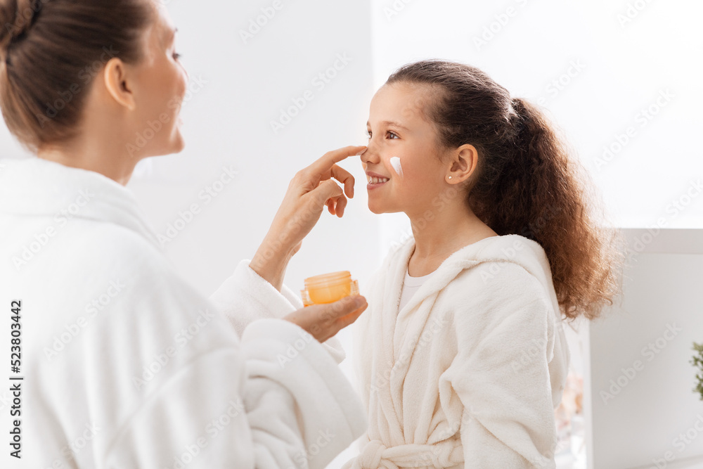 beauty, hygiene, morning and people concept - happy smiling mother and daughter with moisturizer at bathroom beauty, hygiene, morning and people concept - happy smiling mother and daughter with moisturizer at bathroom