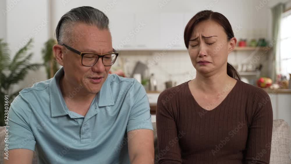 caring asian retired father consoling frustrated daughter and patting on her back in living room at home. the depressed woman cries and buries her face in hands while listening caring asian retired father consoling frustrated daughter and patting on her back in living room at home. the depressed woman cries and buries her face in hands while listening