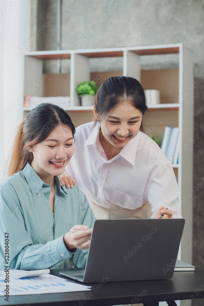 Two young Asian businesswoman discuss investment project working and planning strategy. Business people talking together with laptop computer at office. Two young Asian businesswoman discuss investment project working and planning strategy. Business people talking together with laptop computer at office.