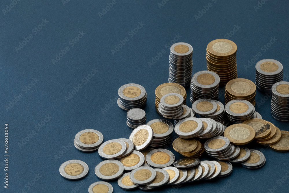 Mexican peso coins, piled up and scattered on a blue colored surface, with copy space Mexican peso coins, piled up and scattered on a blue colored surface, with copy space