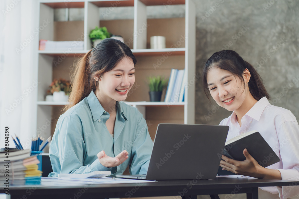 Two young Asian businesswoman discuss investment project working and planning strategy. Business people talking together with laptop computer at office. Two young Asian businesswoman discuss investment project working and planning strategy. Business people talking together with laptop computer at office.