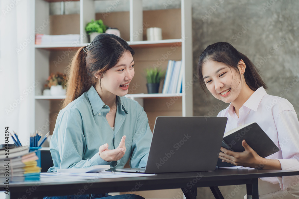 Two young Asian businesswoman discuss investment project working and planning strategy. Business people talking together with laptop computer at office. Two young Asian businesswoman discuss investment project working and planning strategy. Business people talking together with laptop computer at office.