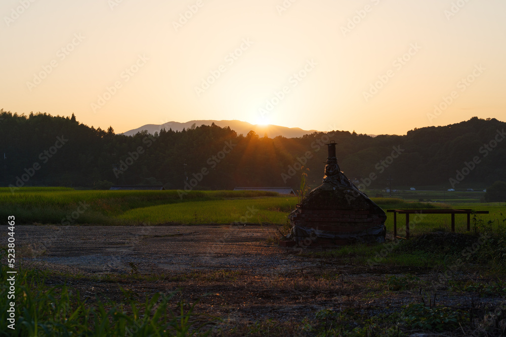 Japanese farm village at dusk, golden fields bathed in the setting sun