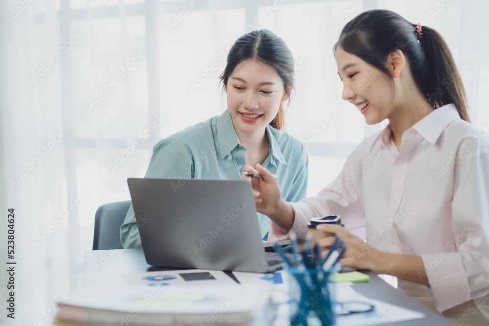 Two young Asian businesswoman discuss investment project working and planning strategy. Business people talking together with laptop computer at office. Two young Asian businesswoman discuss investment project working and planning strategy. Business people talking together with laptop computer at office.
