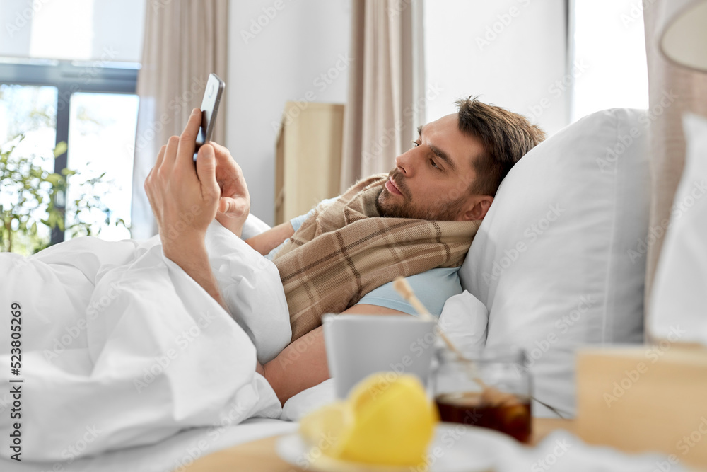 health, illness and people concept - sick man with smartphone in bed at home - obrazy, fototapety, plakaty 