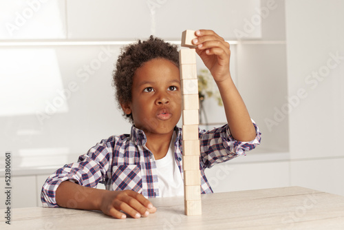 Valokuva Cute clever child small boy playing and building a tower of wooden blocks at hom