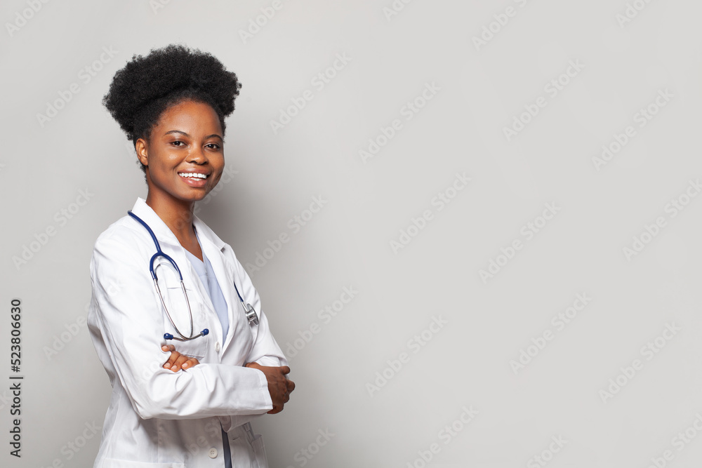 Happy beautiful female doctor in medical coat standing with crossed arms on white banner background Happy beautiful female doctor in medical coat standing with crossed arms on white banner background
