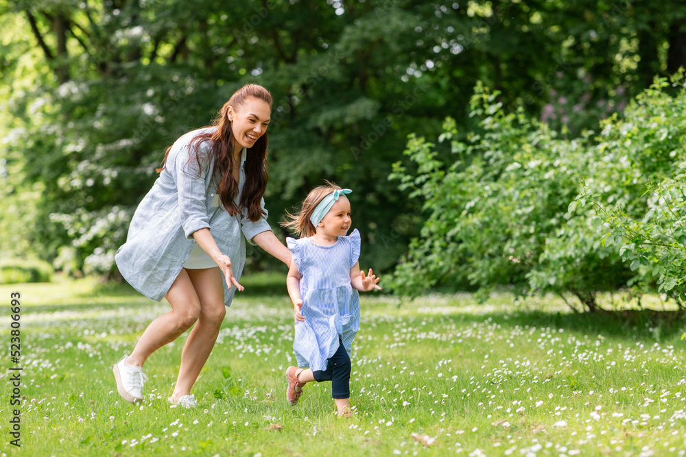 Fototapeta premium family, motherhood and people concept - happy mother with little daughter playing at summer park or garden