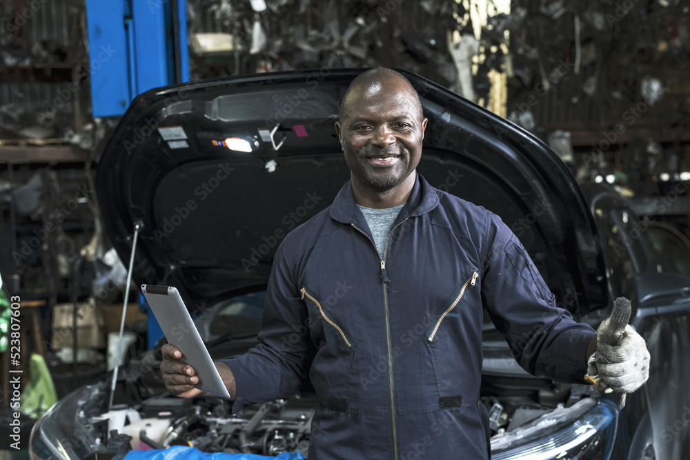 Smiling male African mechanic holding taplet working in auto repair service, 