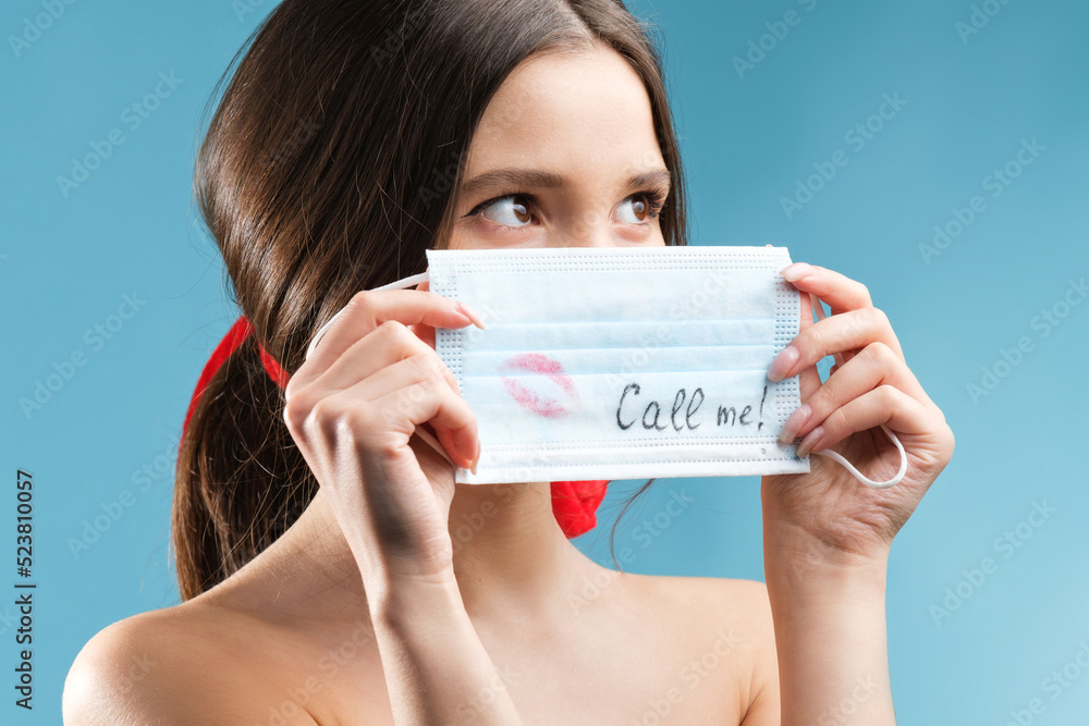 Close up photo of a beautiful lady holding in her hands medical mask with a kiss sign and an inscription covering her face. Close up photo of a beautiful lady holding in her hands medical mask with a kiss sign and an inscription covering her face.