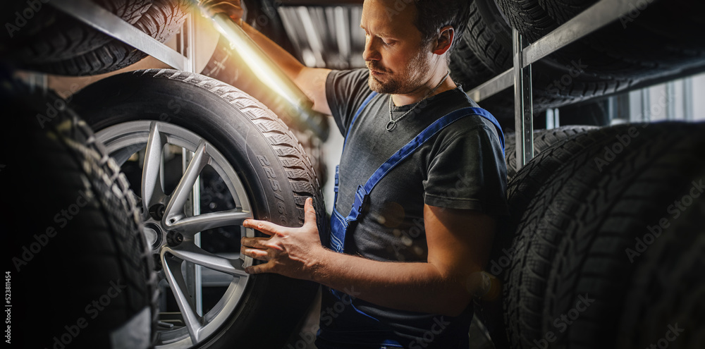 tire at repairing service garage background. Technician man replacing winter and summer tyre for safety road trip. - obrazy, fototapety, plakaty 