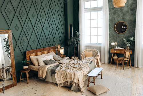 Cozy boho bedroom with wooden furniture, console table, textiles, green walls, large windows and potted plants. Empty space