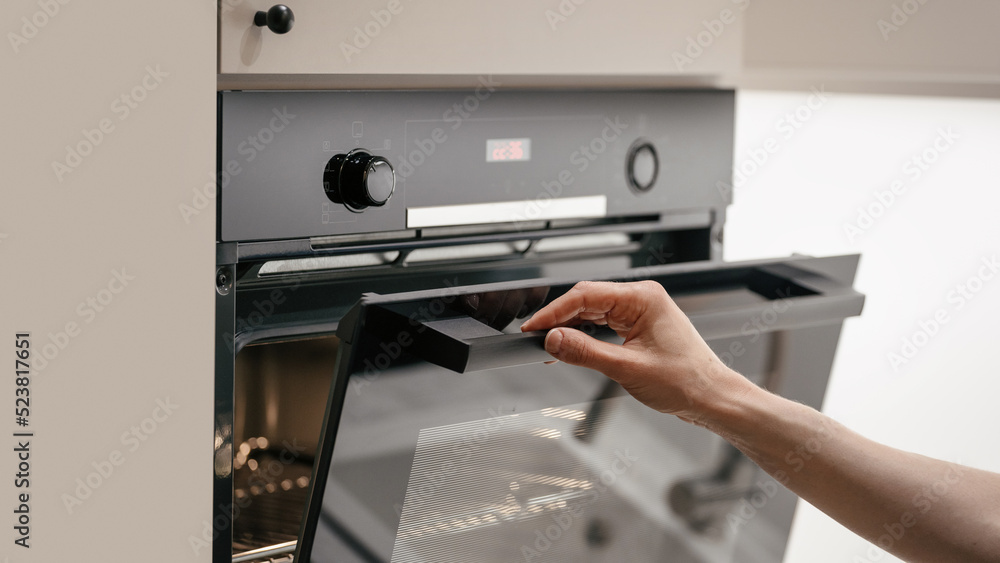 Woman opening glass door in modern electric oven Woman opening glass door in modern electric oven