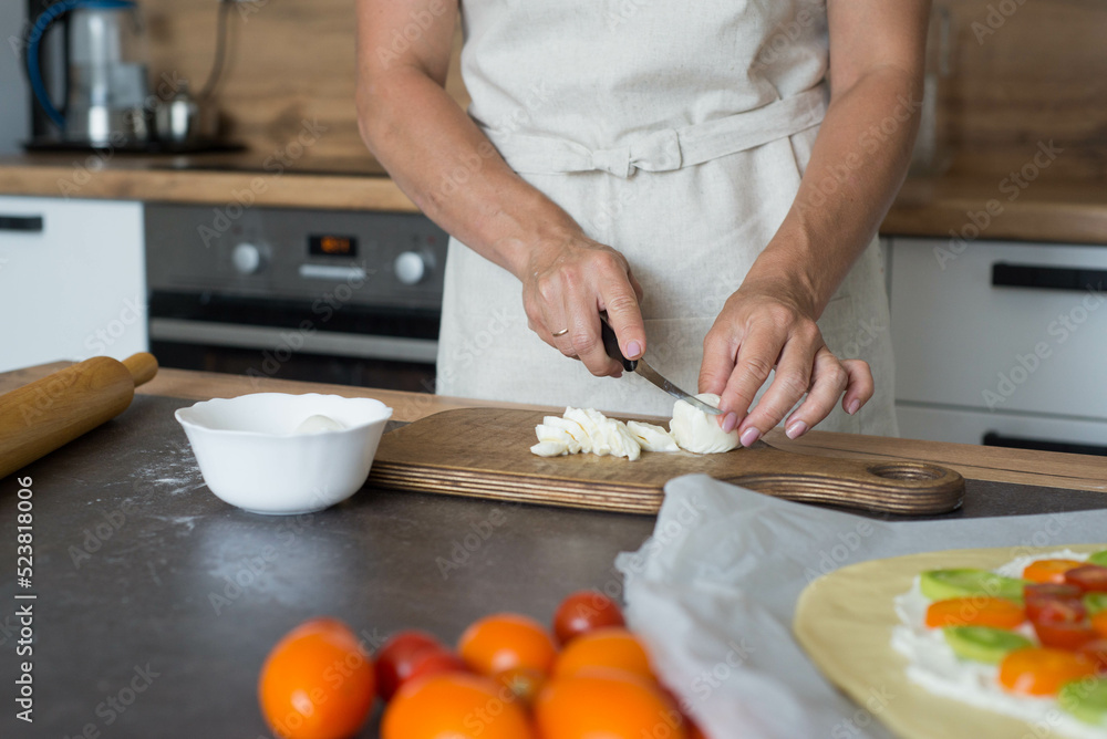 woman hands slicing mozzarella on wooden for pizza in the kitchen. woman hands slicing mozzarella on wooden for pizza in the kitchen.