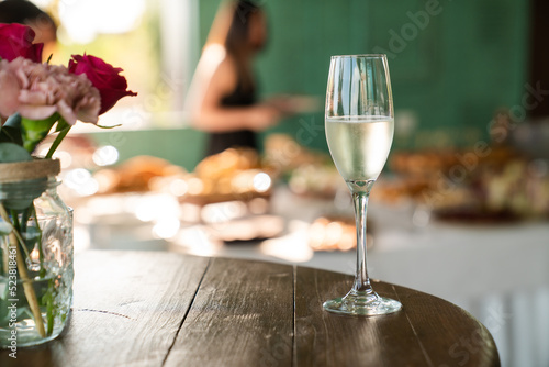 White Wine Glass close-up. Wine glass on table with red roses bouquet and a beautiful buffet in the background.