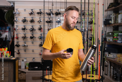 Man angler choosing a thermos in a fishing store