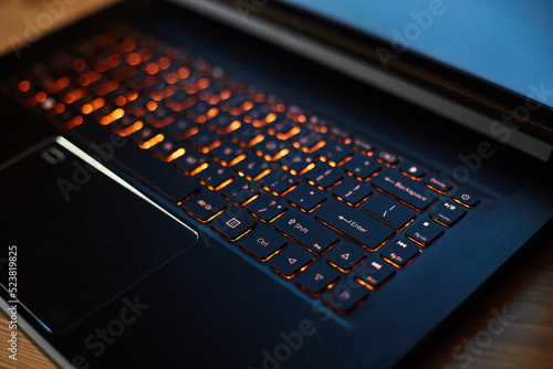 Laptop keyboard with orange neon illumination, backlit keyboard.