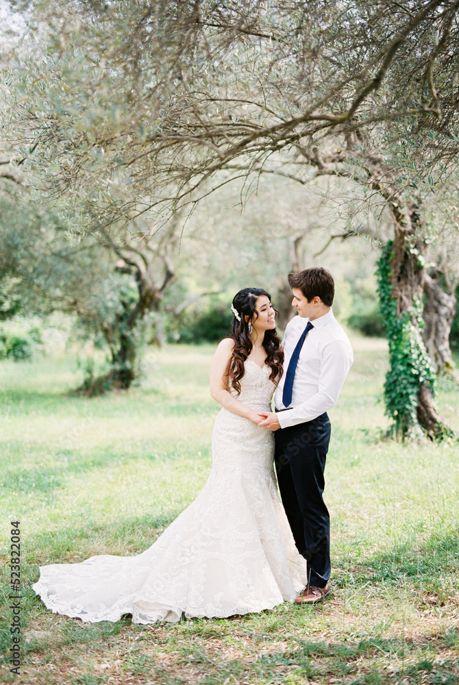 Groom and bride in a white mermaid dress stand under a tree