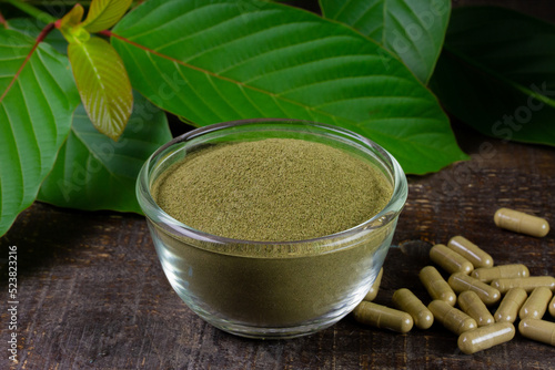 Mitragyna Speciosa Korth or kratom powder on transparent bowl with green leaf and capsules on rustic wooden table. 