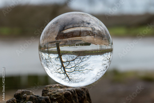 The River Hamble reflected upside down in a crystal ball balanced on a tree branch with the river and countryside blurred in the background