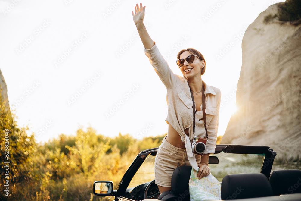 Obraz premium Woman standing in cabriolet on the mountain sunset holding map and camera